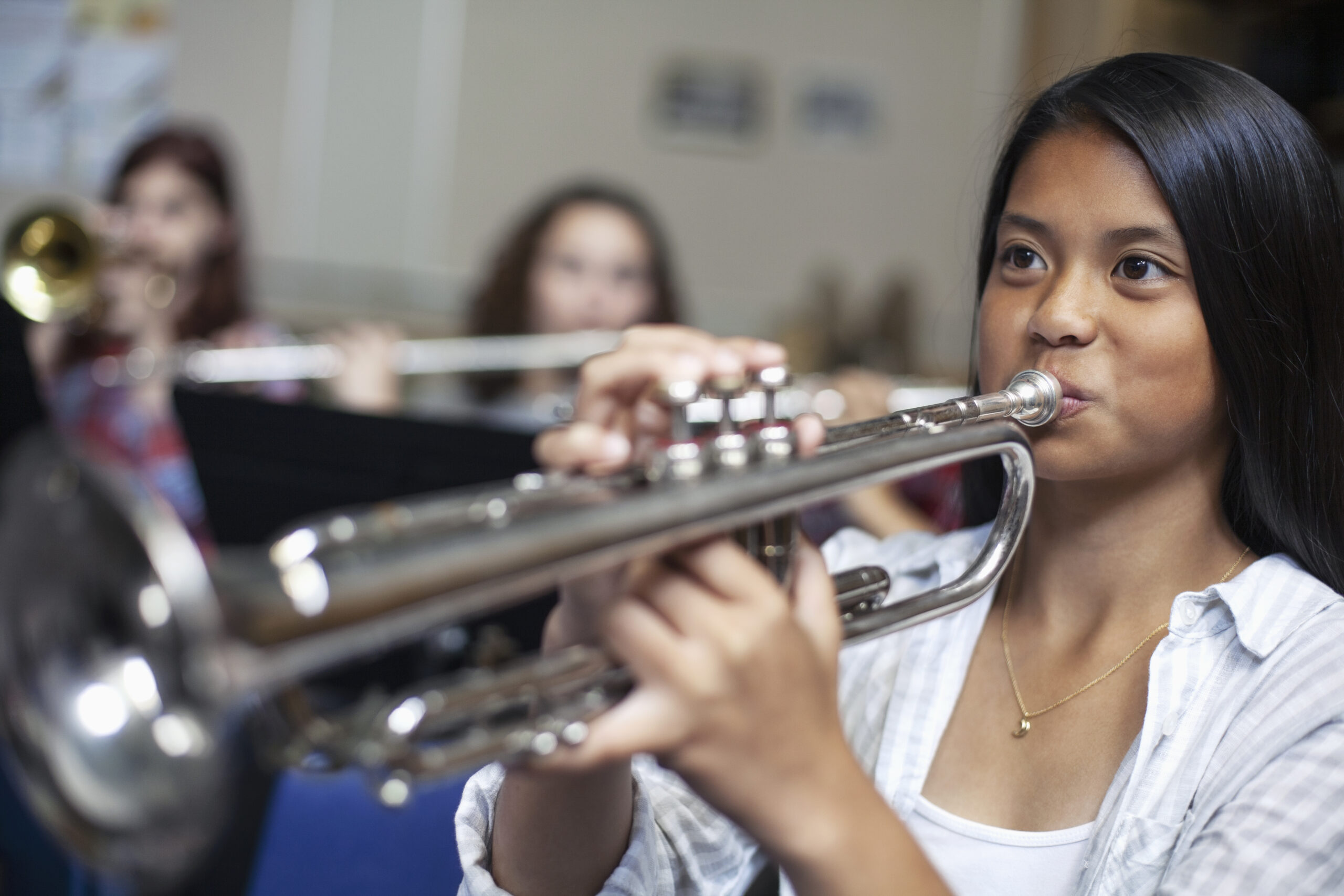 Teenage Asian Filipino girl blowing into trumpet in musical class